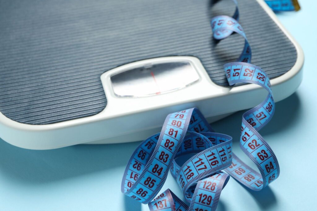 Weight scale with a blue measuring tape, symbolizing tracking progress, fat loss goals, and sustainable weight management.