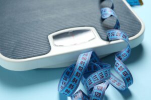 Weight scale with a blue measuring tape, symbolizing tracking progress, fat loss goals, and sustainable weight management.