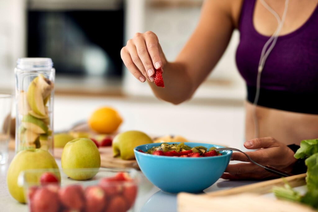 Active woman eating a fresh fruit salad in a bright kitchen, showing healthy eating habits supported by anti-inflammatory weight loss programs in Eau Claire, WI.
