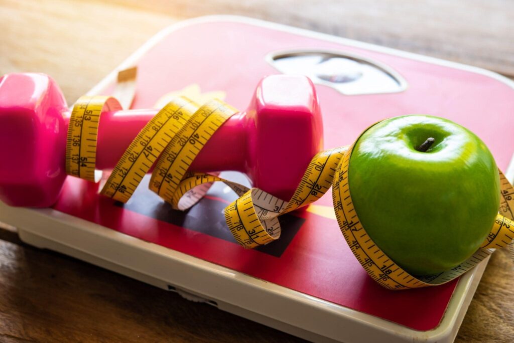 The concept of weight loss with a measuring tape wrapped around exercise equipment and an apple.