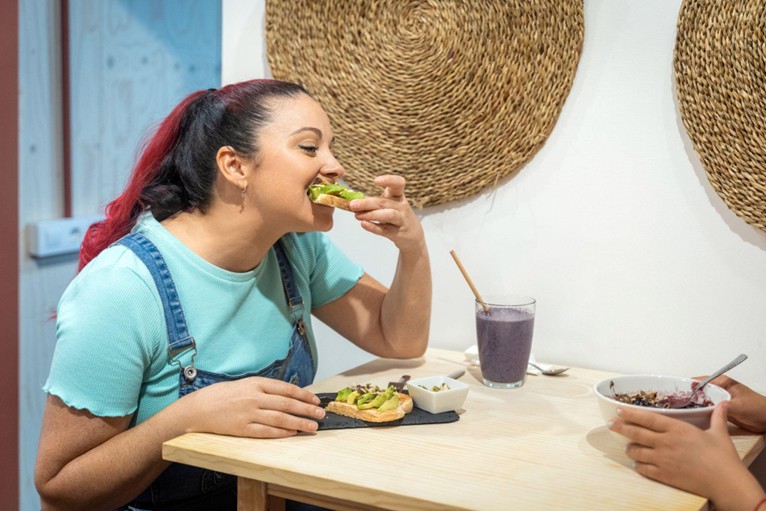 Woman eating avocado toast while having breakfast with a friend in a cafe.