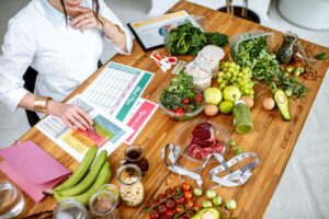Nutrition coach creating a weekly meal plan with fresh produce, lean proteins, and a diet chart — showing practical meal planning ideas offered by River Valley Weight Loss clinics.