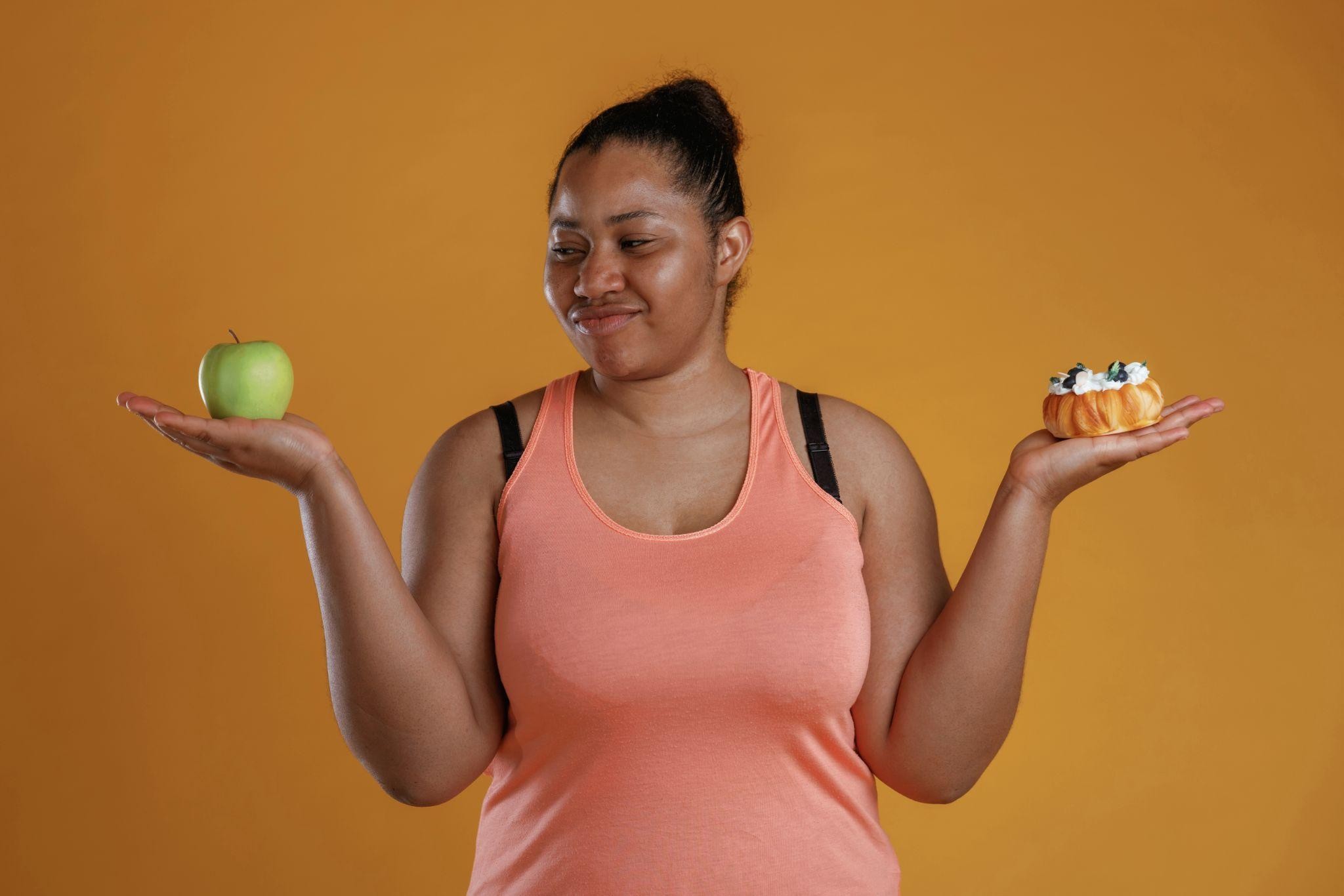 Woman comparing an apple and a pastry, symbolizing diet choices before starting a metabolic reset method at a Wisconsin weight loss center.