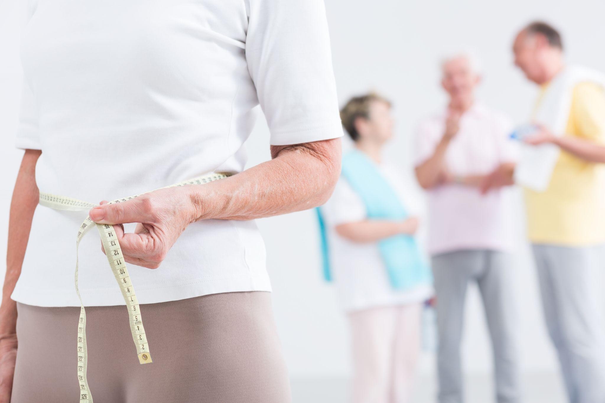 Midlife woman measuring waistline as part of metabolic health and weight loss program at a wellness center.