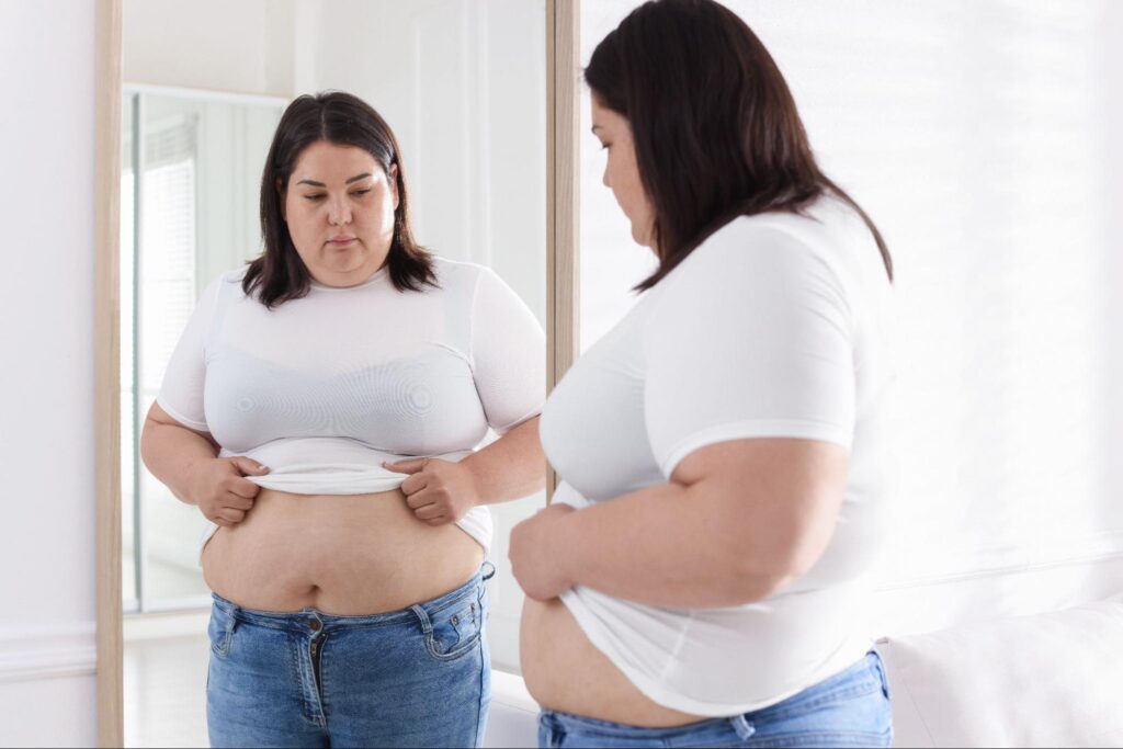 Woman looking in a mirror, feeling frustrated about weight loss plateau.